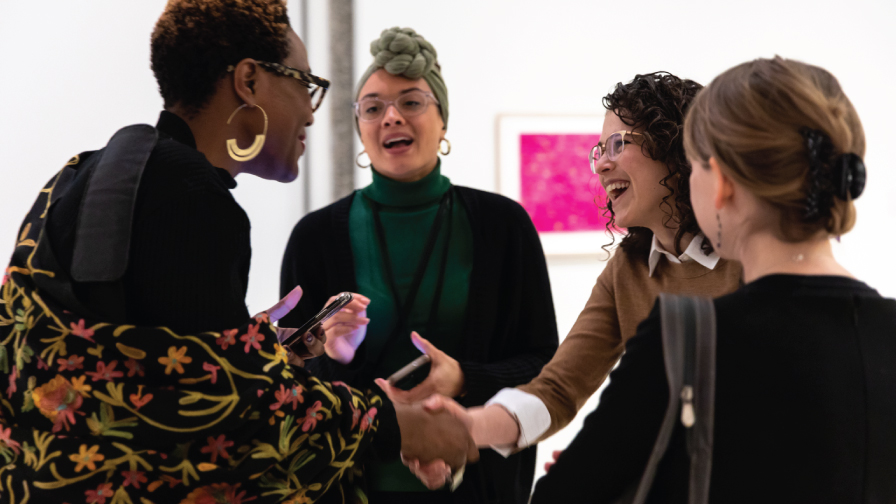 Four women talk, while two of the women shake hands.
