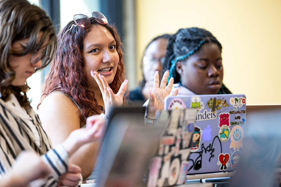 Students in a classroom, one making a hand gesture while speaking
