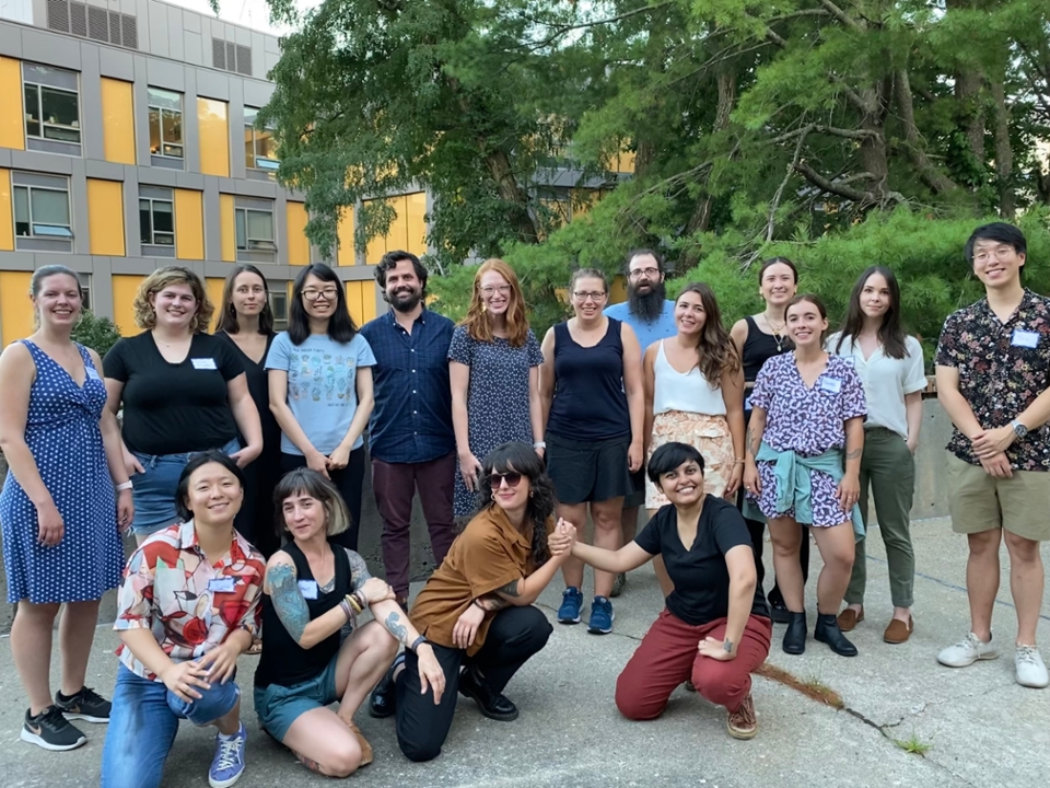 Grad students with name tags on smile for the camera outside in front of some trees