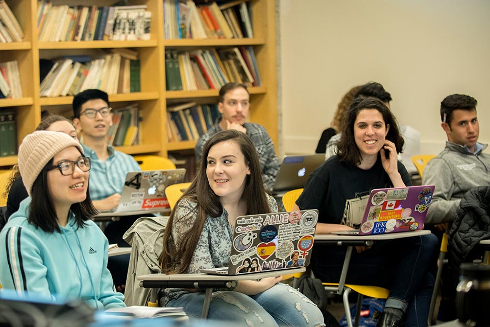 Students sitting in classroom desks with open laptops.