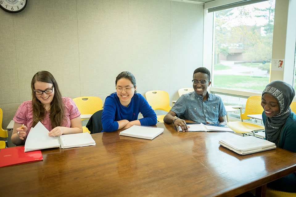 Four smiling students sitting around a table with notebooks in front of them. 