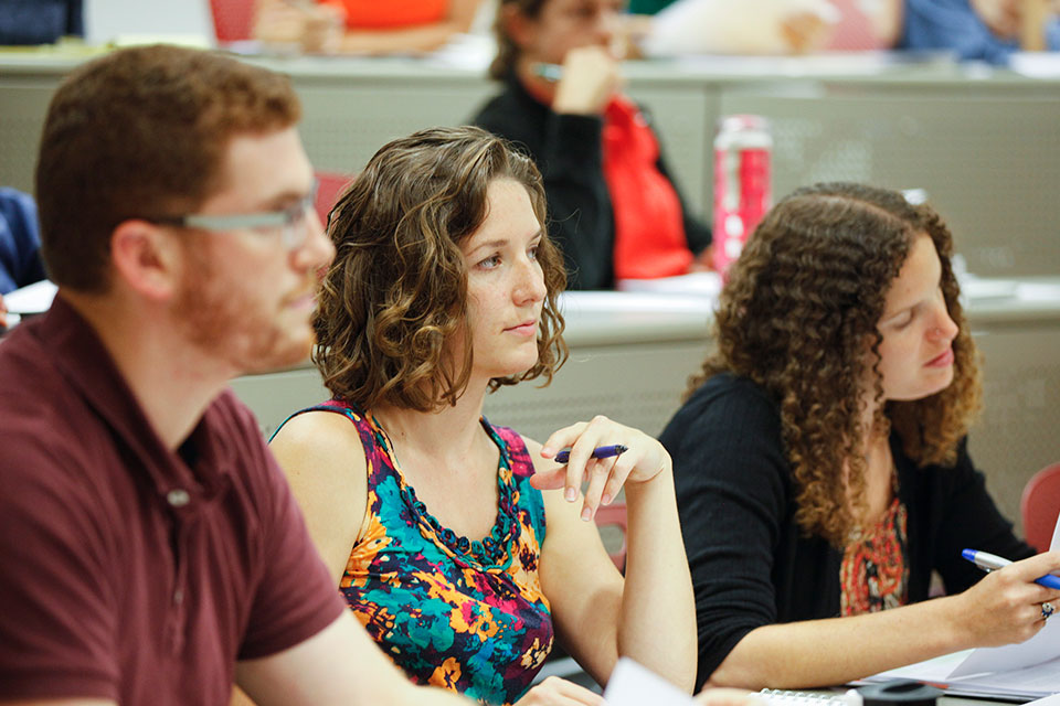 Two students look to the front of the classroom while one refers to her notes