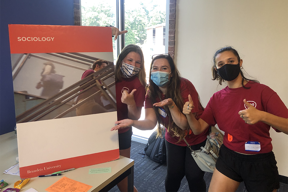 Three UDRs in masks hold a poster that says "Sociology" at the top