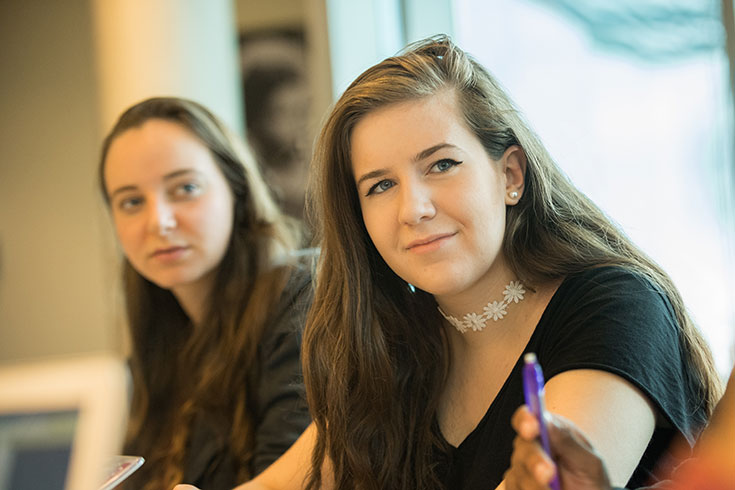 A student smiles slightly as she looks to another member of the class