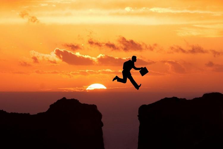 person jumping over canyon with briefcase