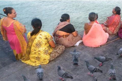 Group of women in India sitting by water joined by pigeons