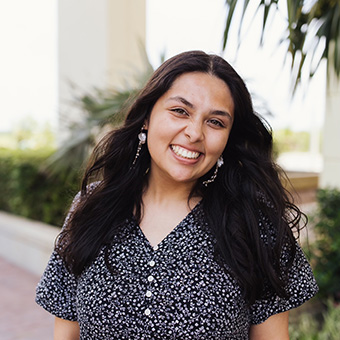 an image of a woman with long dark hair smiling broadly while tilting her head, with a palm tree behind her