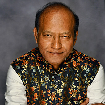 headshot of a smiling Indian man with colorful shirt and white sleeves
