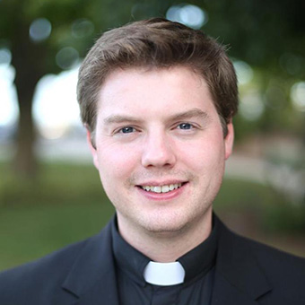 close up headshot of a smiling young white man in a priest collar