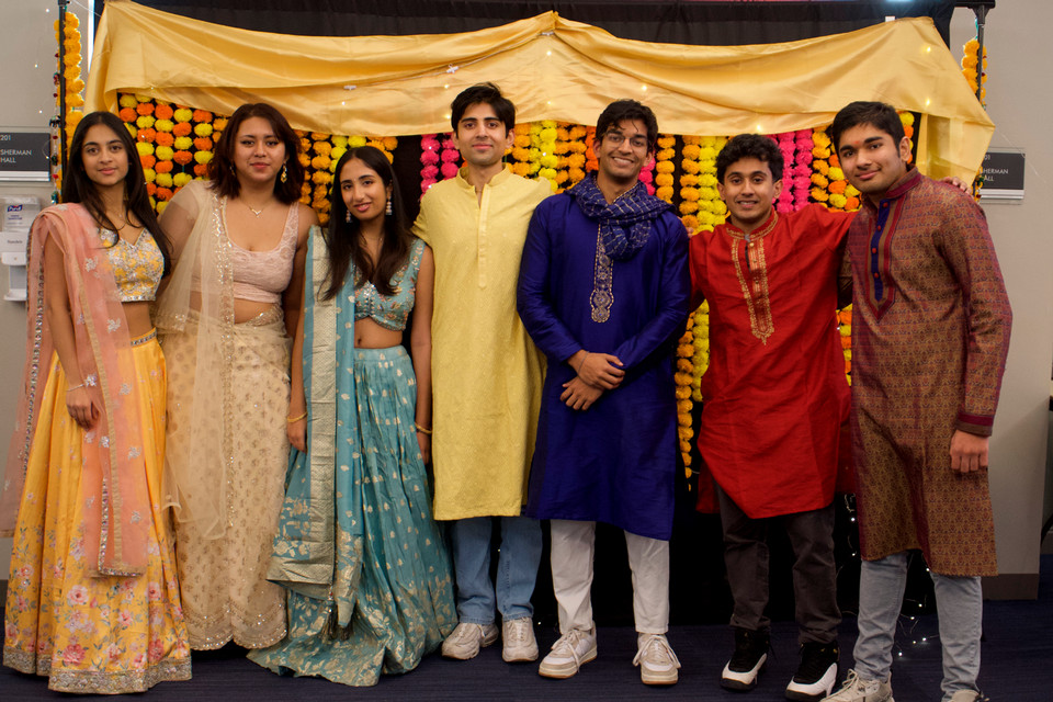 a group of male and female students dressed in traditional Indian dress standing in a line and smiling at the camera