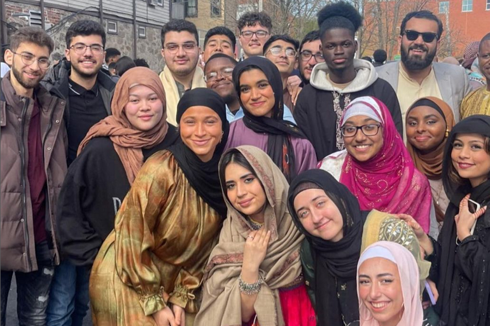 a group of students outside packed in close, squatting down and standing up, smiing and glowing into the camera, women in hijabs