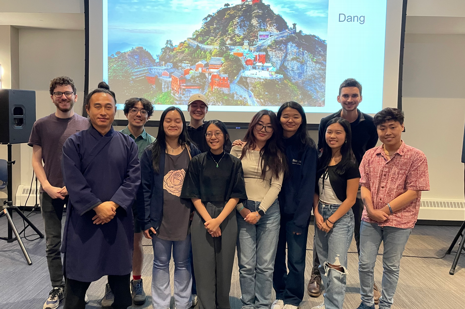 a group of students and a martial arts man standing in front of a screen with an image of a Chinese village