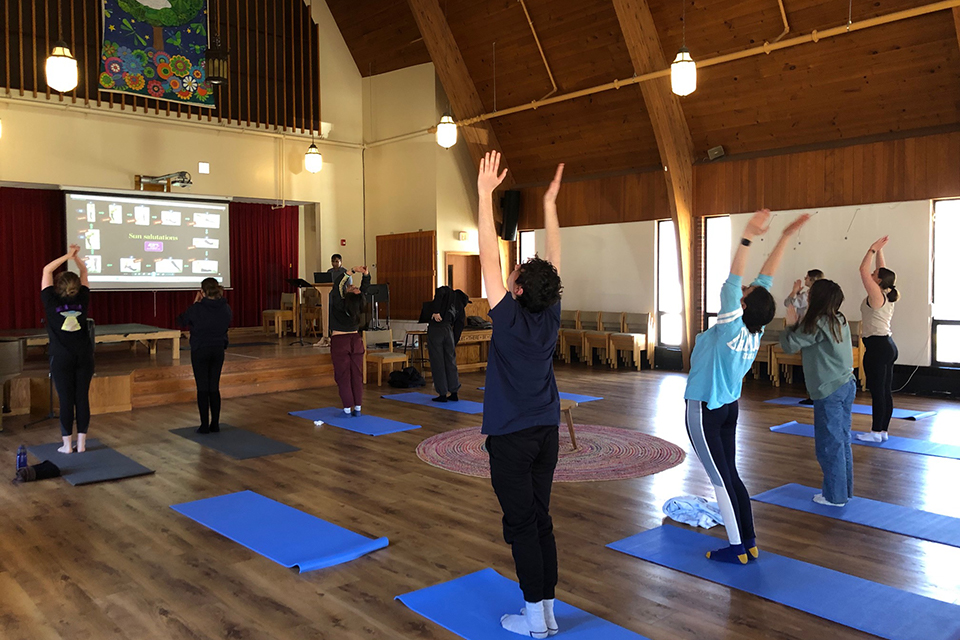 students standing in upright yoga stretch in large room, facing forward