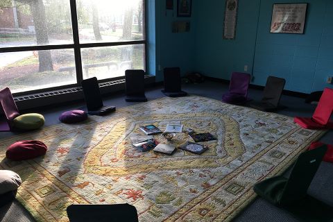 photo of a room with flapjacks - small legless seats with a back - in a circle on a rug with a small centerpiece with rocks and tall windows in the back