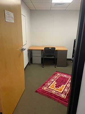 Looking into a room with a desk and a prayer rug