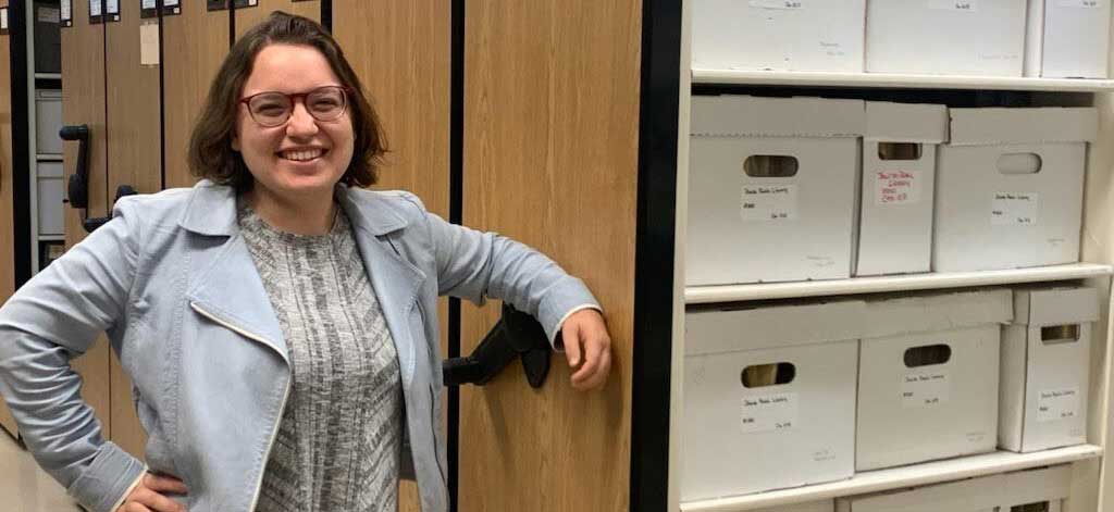 Dina leans against the stacks containing archival files