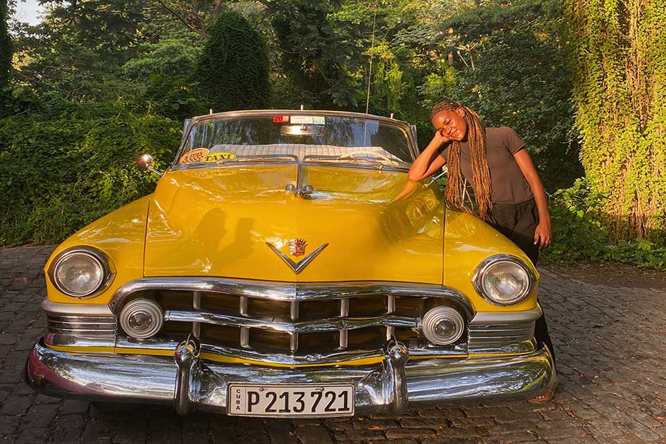 Mishara Nozea leans on an old yellow convertible