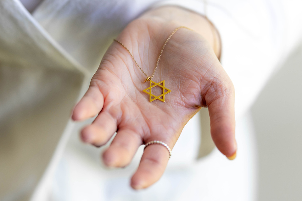 A hand holds a gold Star of David necklace