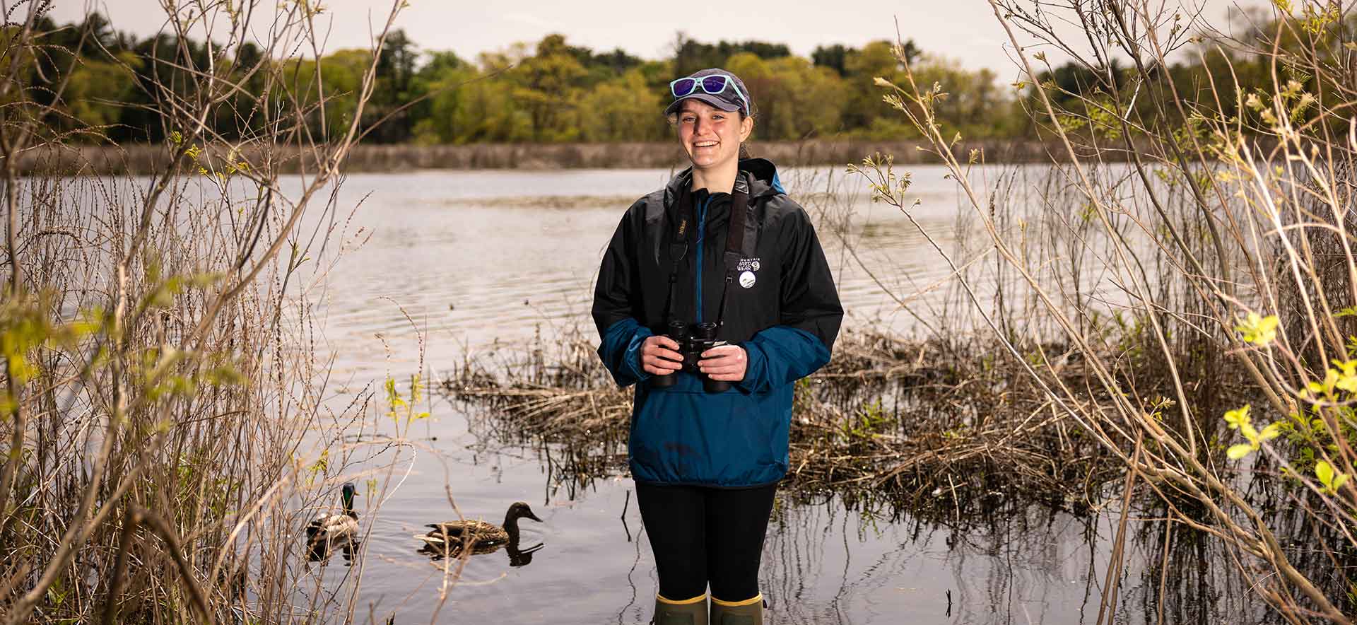 Kate stands in water with ducks behind her