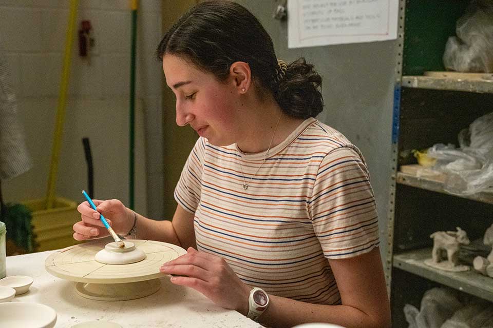A student glazes their pottery
