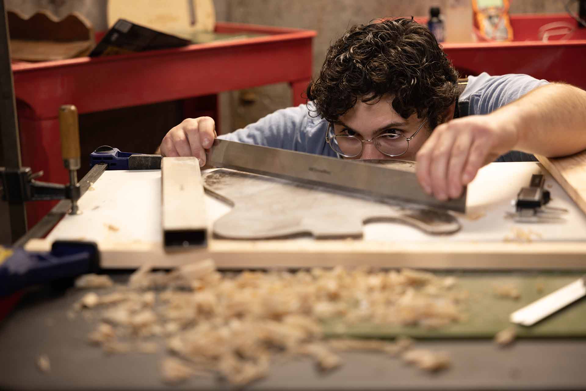 Sam, eye-level with a table, measures pieces for a guitar