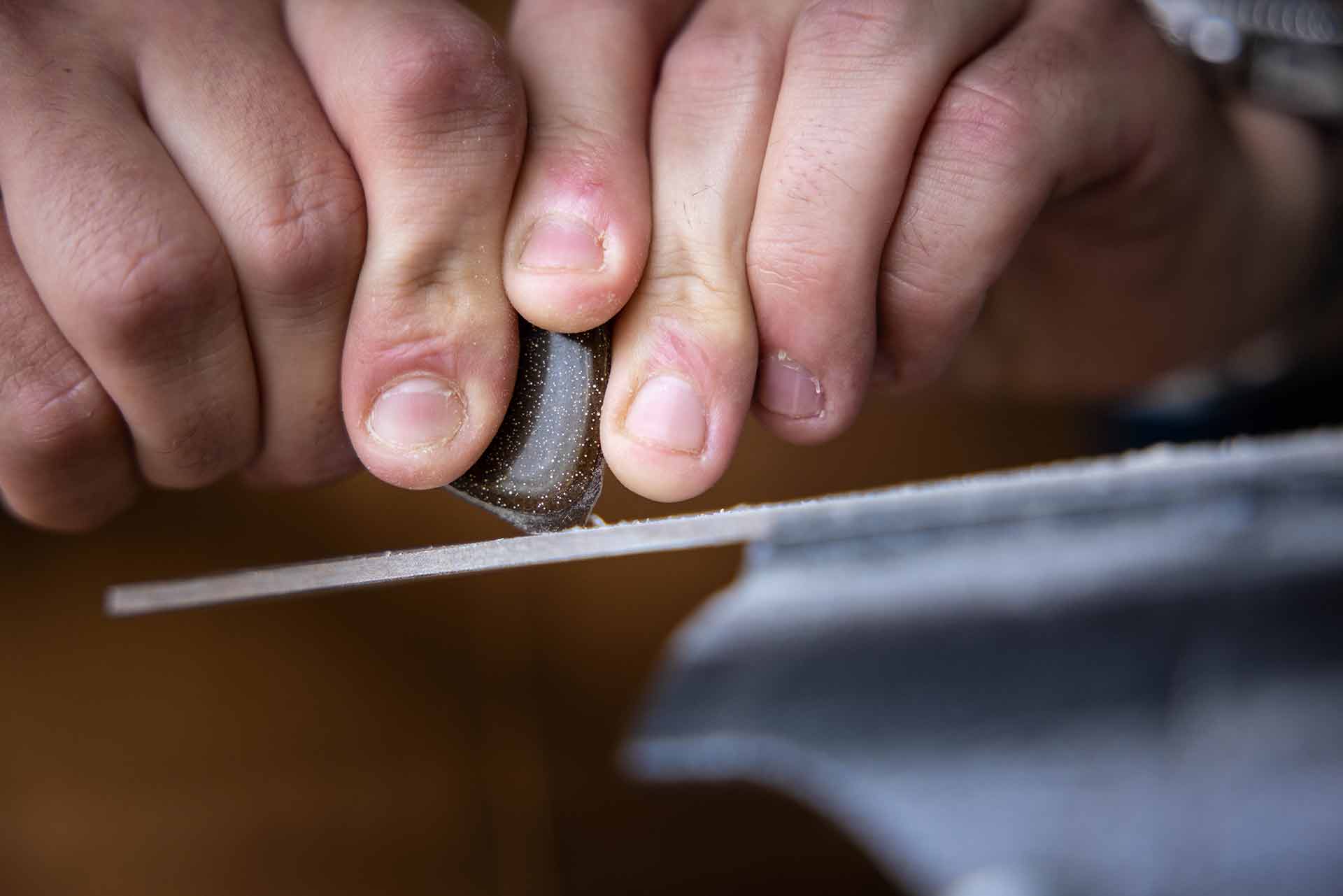 A close up of two hands gripping a guitar pick, sanding it down