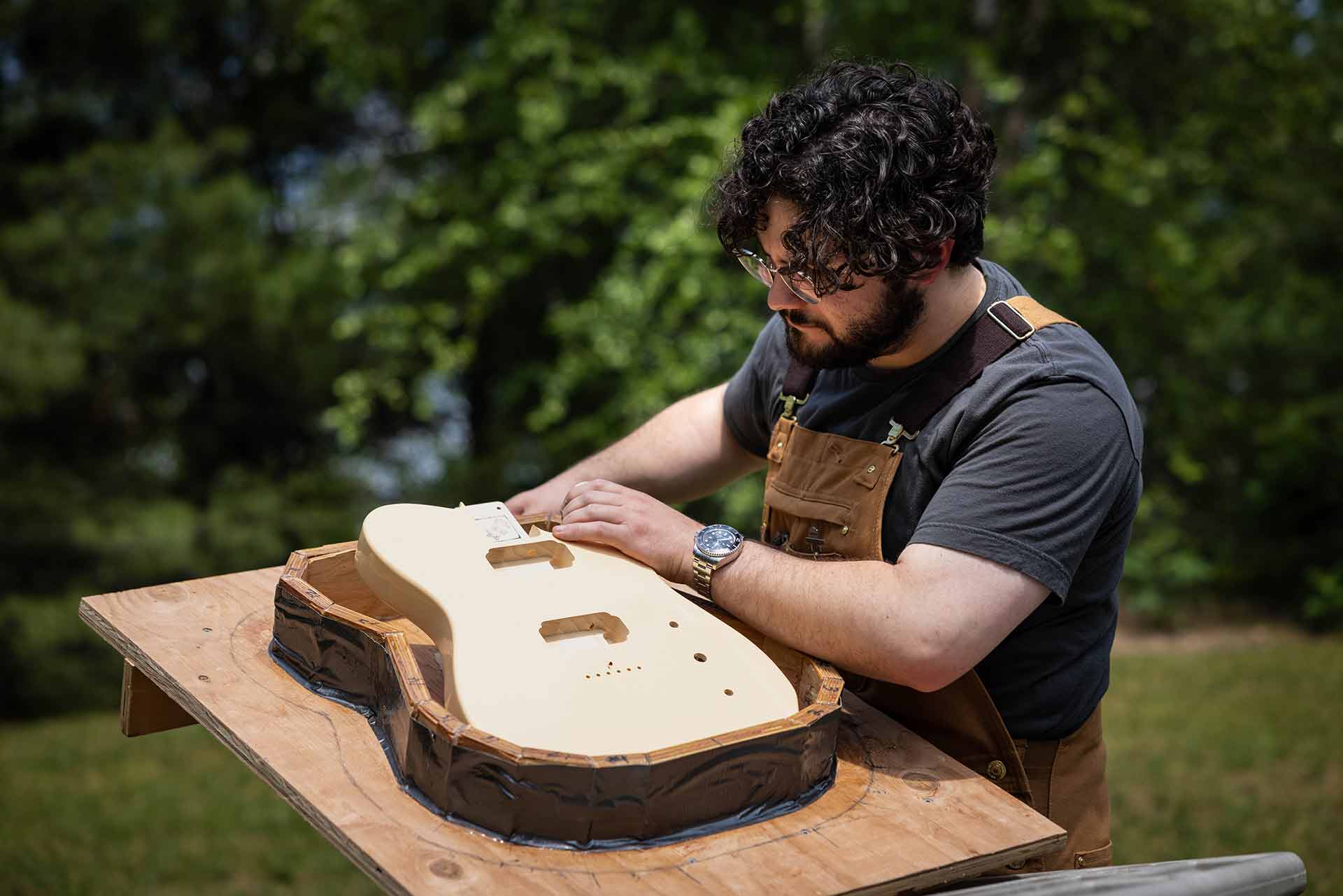 Outdoors, Sam gently places a carved guitar bout inside a template.