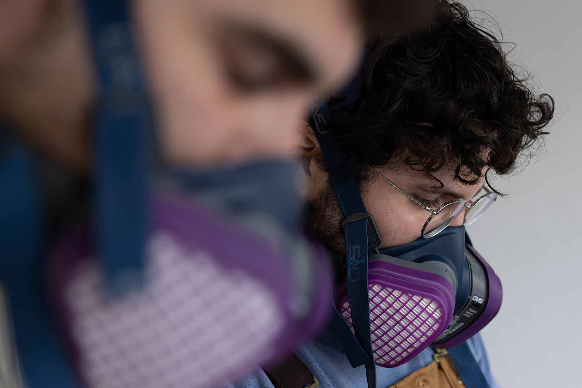 Two people looking downward, purple and gray respirator masks cover their noses and mouths