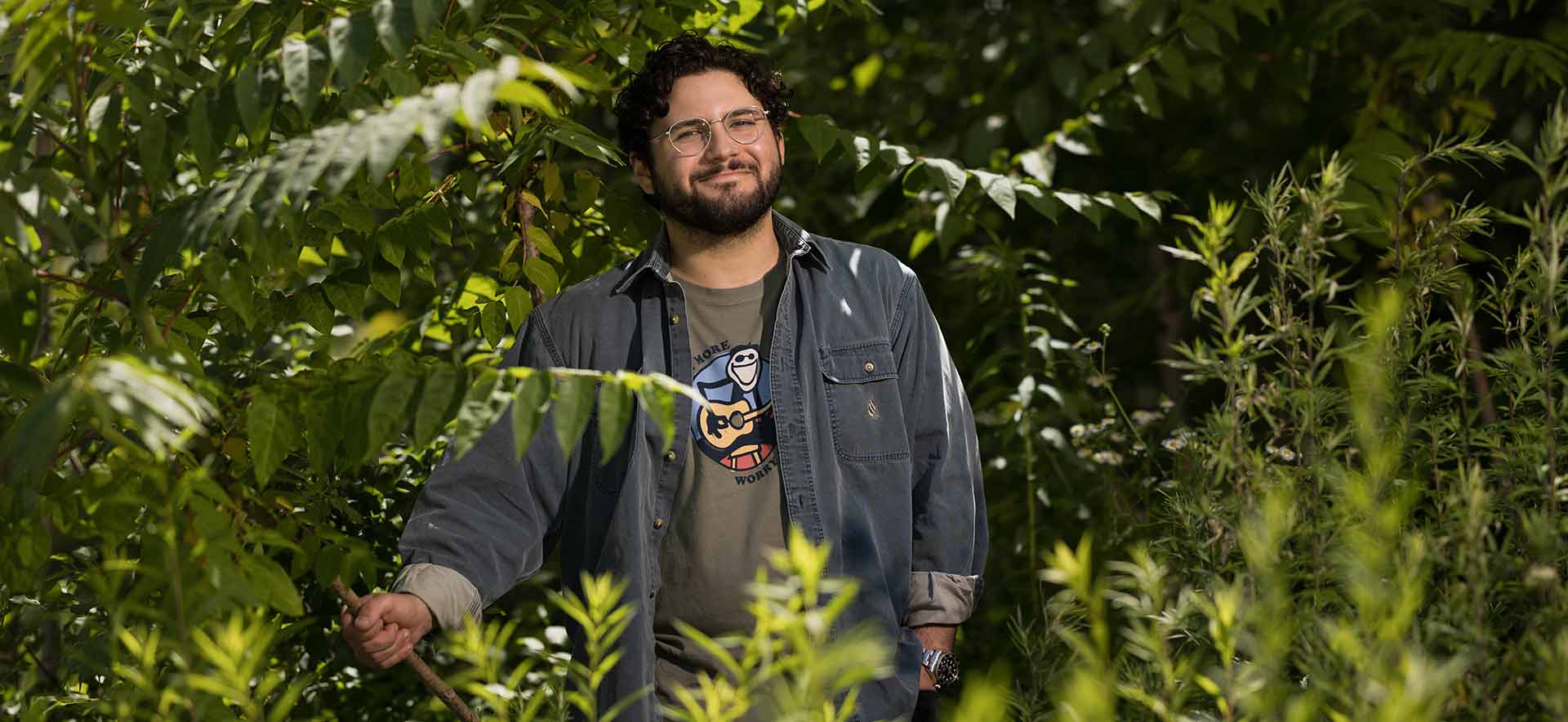 Sam Aronson smiles and poses for a portrait among the invasive species tree of heaven