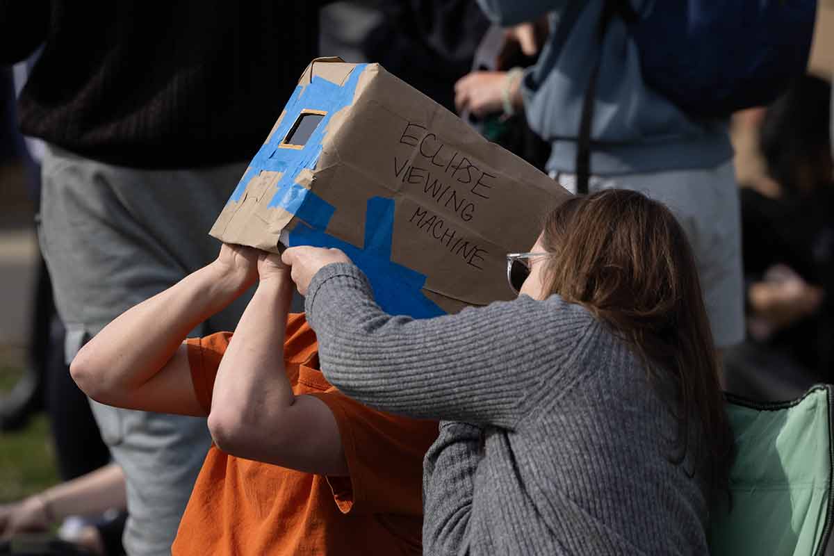 Person with a box on their head, text reads "‘eclipse viewing machine’ on the side"