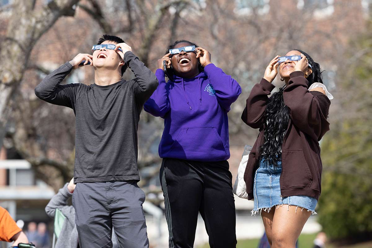 Three students wearing solar eclipse glasses and smiling