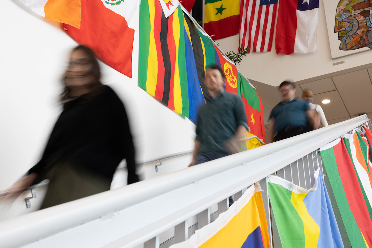 Three blurred students walk down a stairway past flags from many countries.