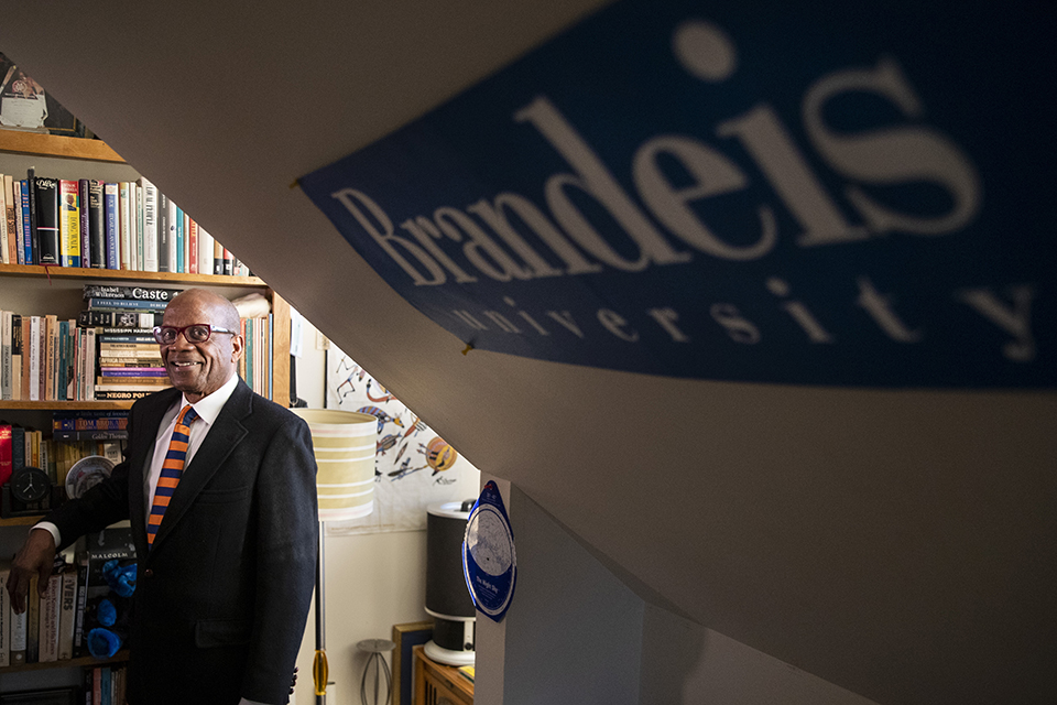 Roy DeBarry smiling in a room with a Brandeis University flag on the wall