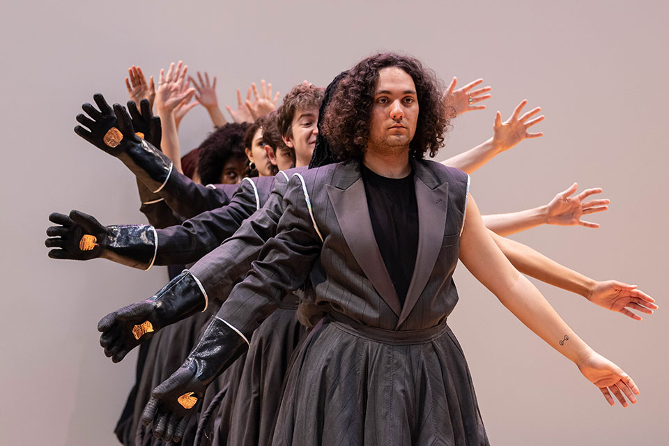 Dancers stand in a line and move their arms up and down.