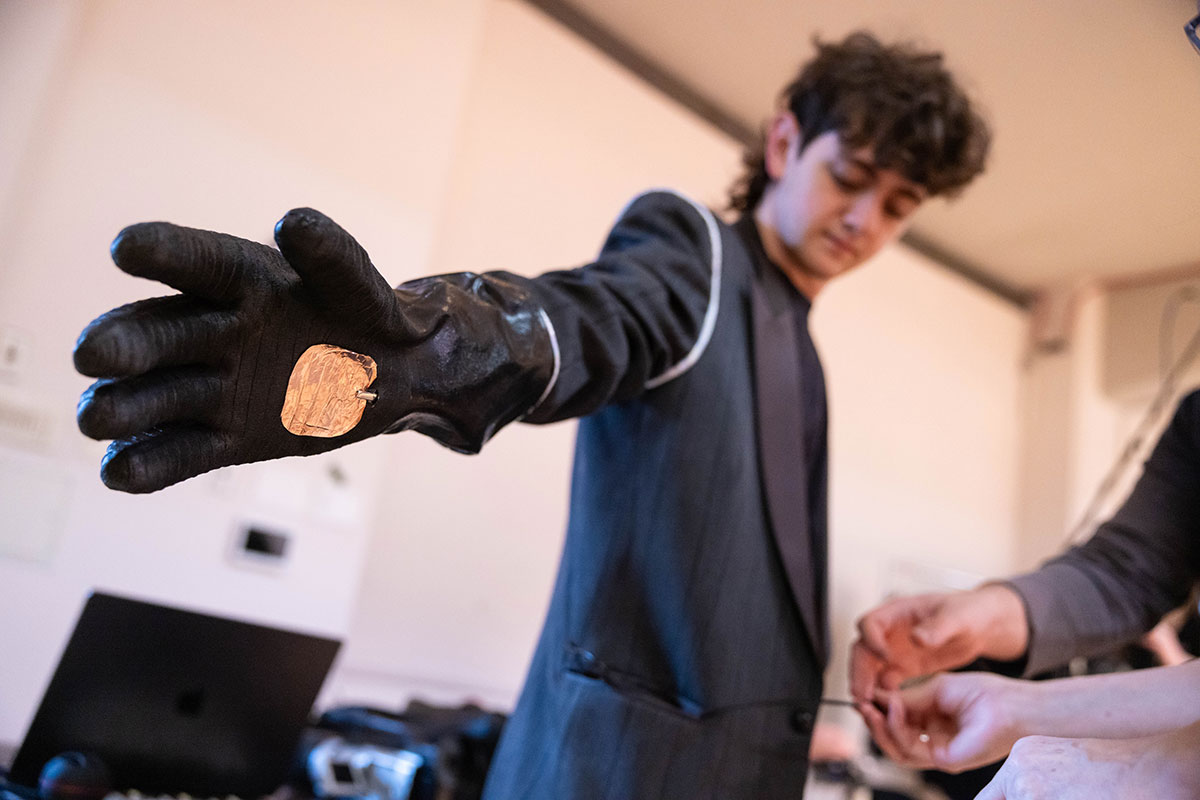 A student holds their arms out while someone fits them with a homemade sensory augmentation device. 