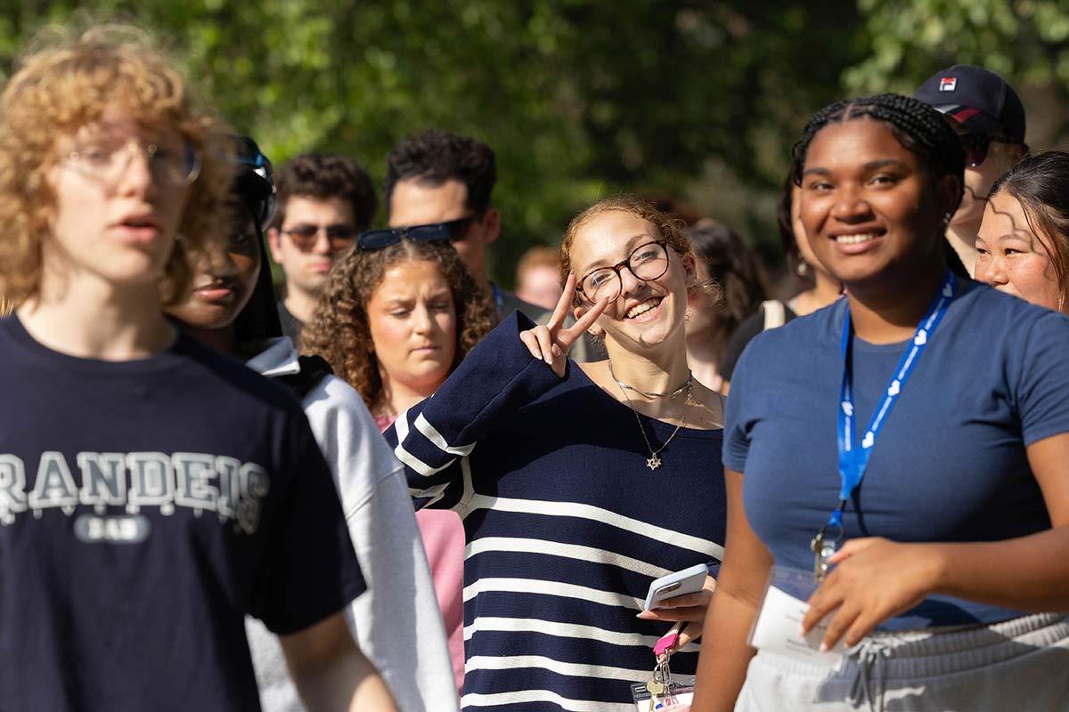 Students walking around campus smiling, one giving the peace sign