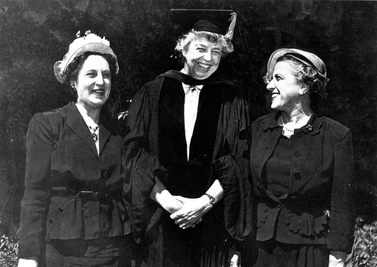 Eleanor Roosevelt wears a cap and gown and stands smiling between two other women.
