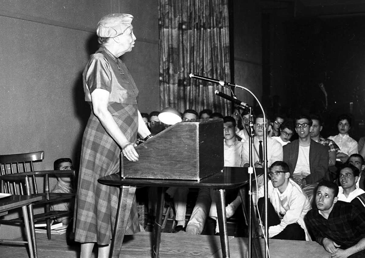 Eleanor Roosevelt stands in front of a podium giving a lecture to a group of students.
