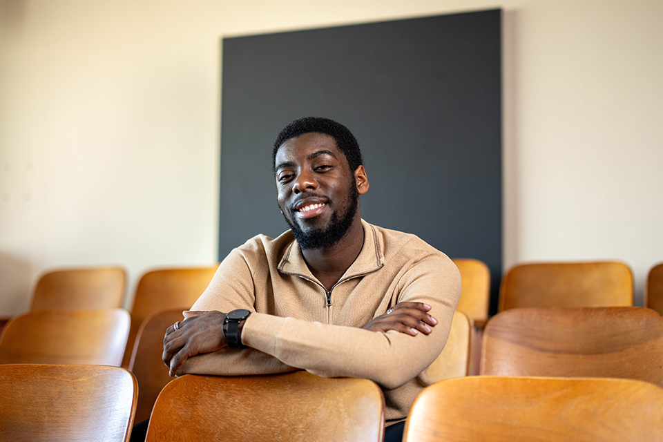 Zaire Simmonds sits with his arms crossed on the back of a wooden chair in rows of lecture hall chairs