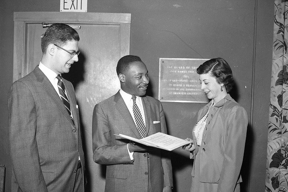 Martin Luther King Jr. stands smiling with two people and presents a document to a woman.