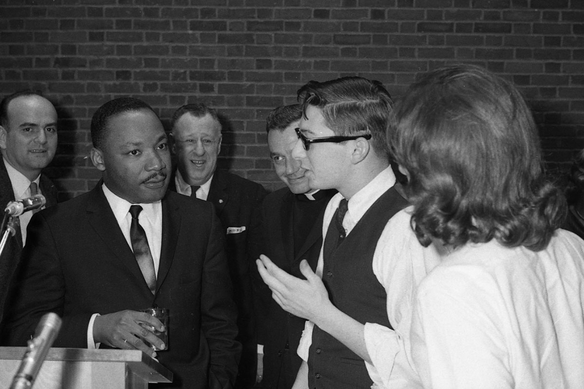 Martin Luther King Jr. engages in conversation with two people while three men look on.
