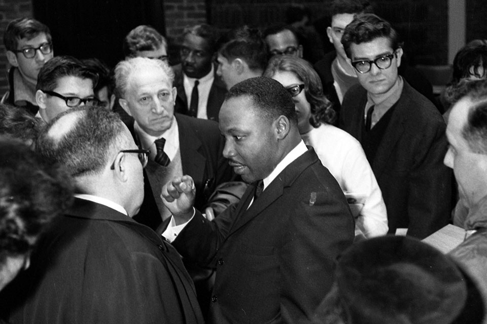 Martin Luther King Jr. stands in a crowd of people and talks to a man.