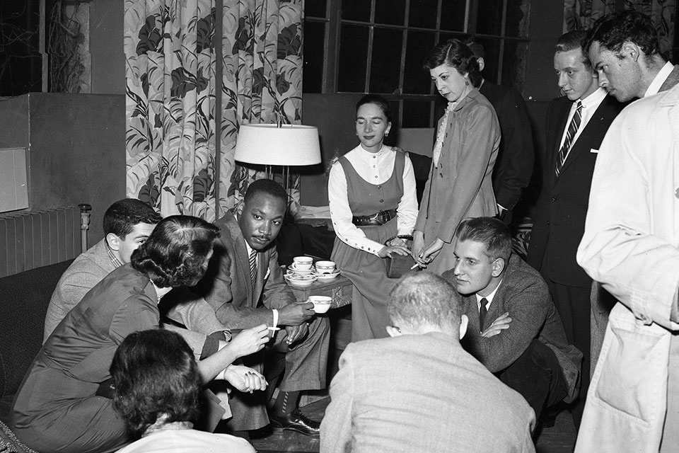 A group of students sit in a living room with Martin Luther King Jr., deep in conversation.