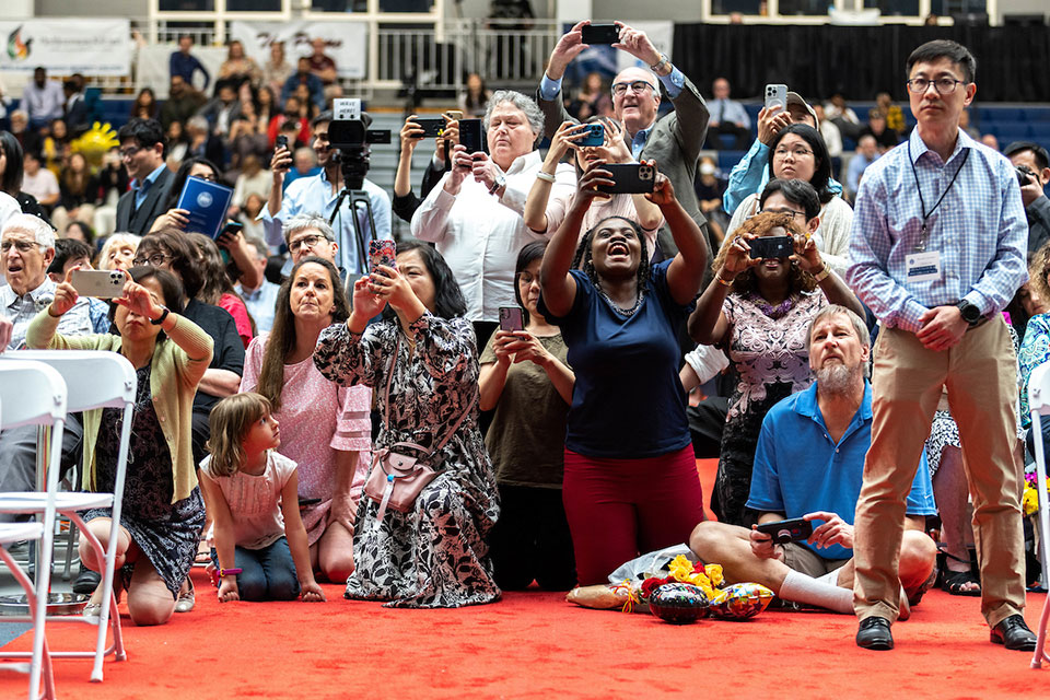 A group of family members stand, kneel and jockey for photos of their graduates.