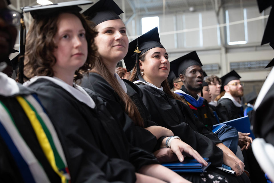 Several graduates in caps and gowns look into the distance