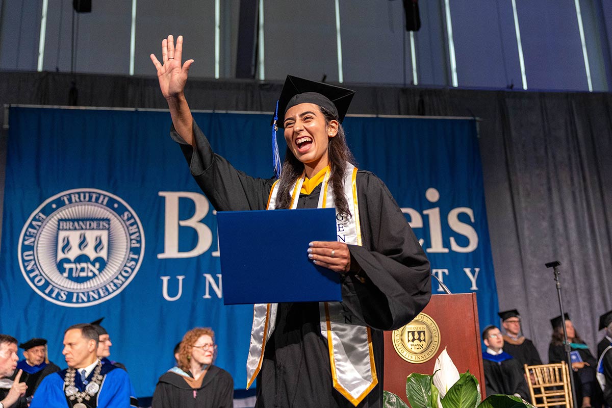 A graduate raises her hand in the air while walking across the stage