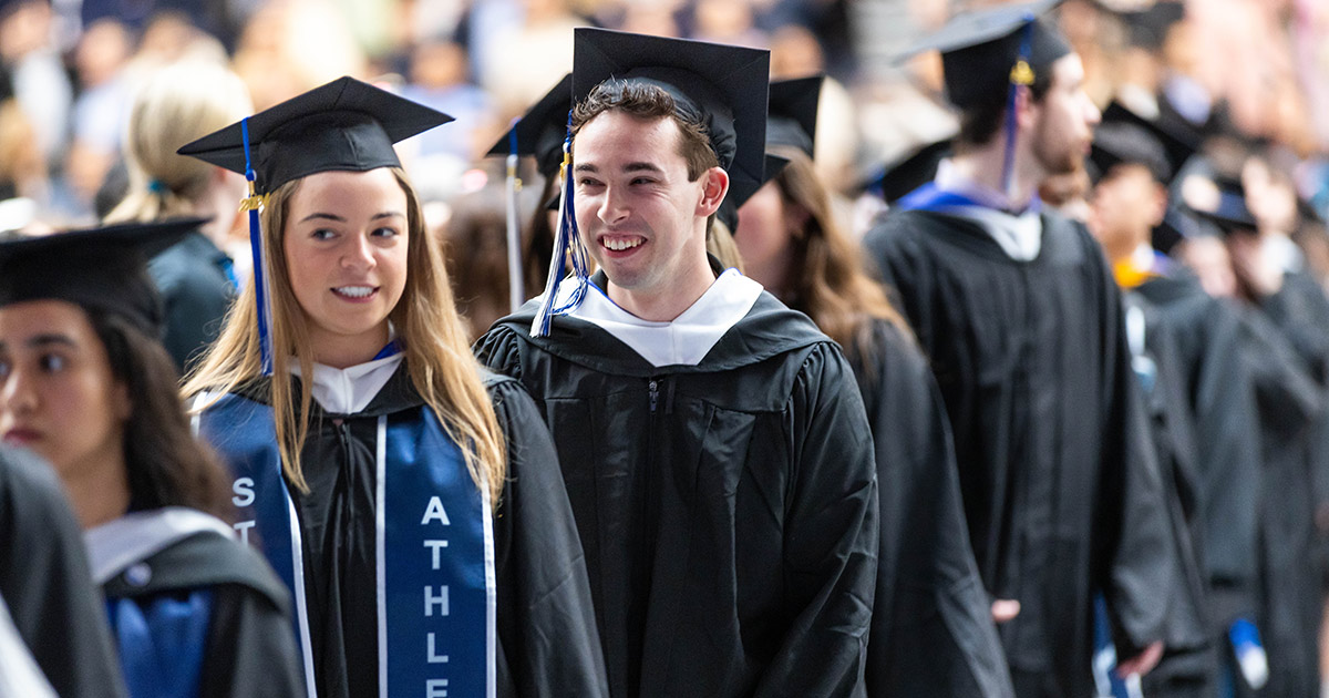 A group of graduates wearing Commencement attire stand in line, smiling.