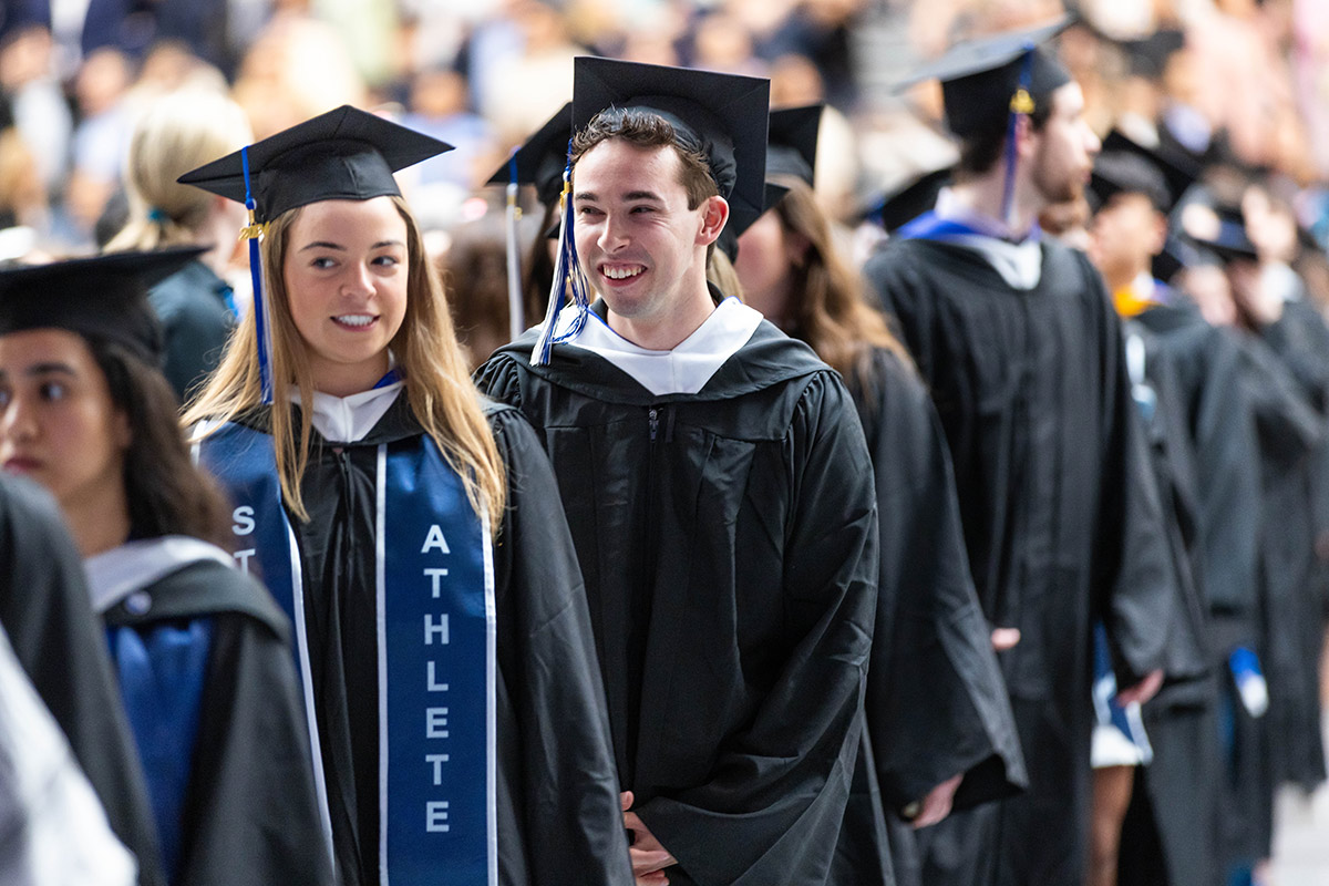 A group of graduates wearing Commencement attire stand in line, smiling.