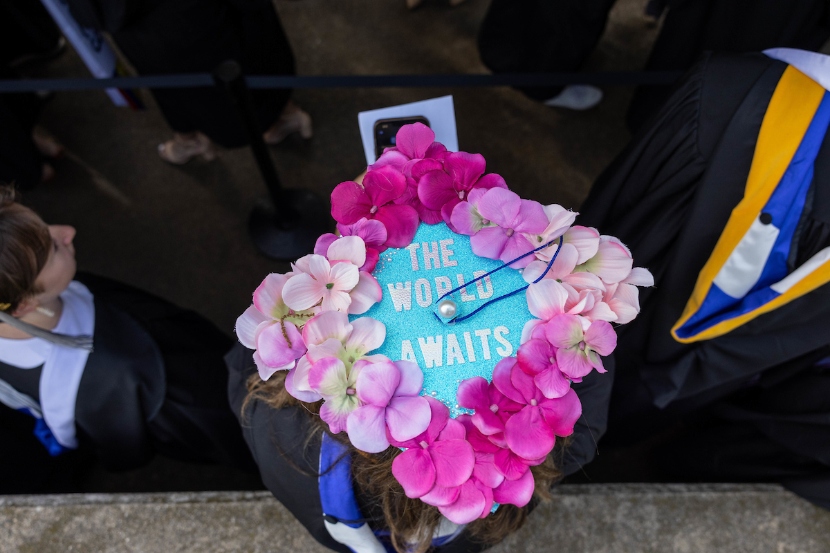 A mortarboard decorated with flowers and text reading "The World Awaits"