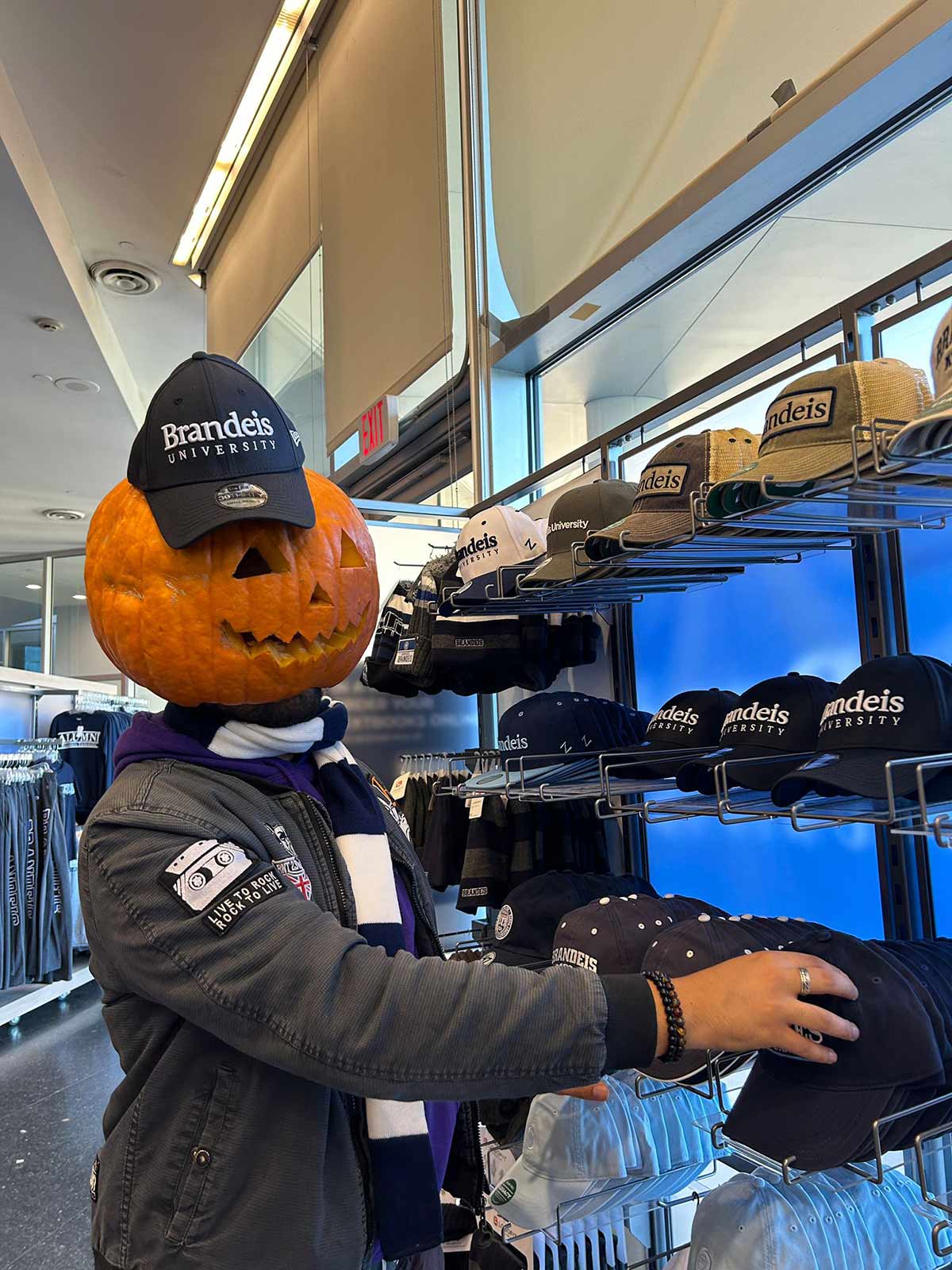 A person wearing a pumpkin on their head checking out some Brandeis hats.